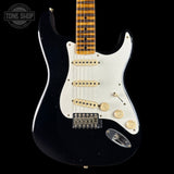 Black electric guitar with a white pickguard on a black background, featuring 'Tone Shop' branding.