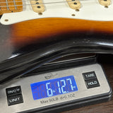 Digital scale displaying weight of a guitar neck on a wooden surface