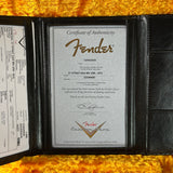 Fender certificate of authenticity in a black leather holder on a yellow background