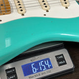 Turquoise electric guitar on a digital scale displaying weight.
