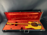 Yellow bass guitar in an open red-lined case on a dark background