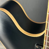 Close-up of a black acoustic guitar with a gold rim on a dark background