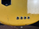 Close-up of a yellow guitar with four tuning pegs on a dark surface