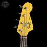 Close-up of a Fender Musicmaster Bass headstock in a natural maple finish, showing four silver tuning pegs and strings against a black background.