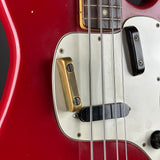 Close-up of a red electric bass guitar showing the white pickguard, gold and black pickups, metal strings, and part of the fretboard.
