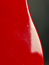 Close-up of a glossy red curved surface with visible scratches and scuffs against a dark gray background.