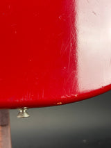 Close-up of a red painted metal surface with visible scratches and a small silver knob, against a dark gray background.