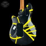A black electric guitar body with bold yellow tape-like stripes, shown from the back against a black background. A wooden neck is visible at the top, and a Tone Shop watermark appears in the upper left corner.