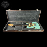 Turquoise electric guitar in an open case with 'Tone Shop' branding.