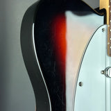 Close-up of the side body of an electric guitar showing a glossy black-to-brown sunburst finish, a white pickguard, and a silver control knob against a gray background.