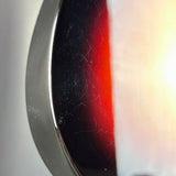 Extreme close-up of a circular product edge, showing a dark black-to-red gradient surface with visible scratches and a bright white light source on the right.