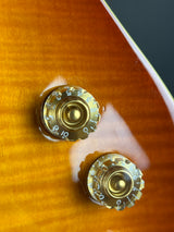 Close-up of two gold-toned guitar volume control knobs on a glossy sunburst wood body.