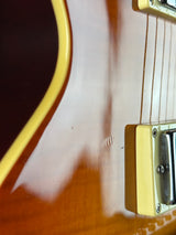 Close-up of a glossy brown electric guitar body with cream pickguard and part of the neck visible.