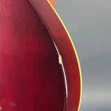 Close-up of the edge of a glossy dark red wooden guitar body with a thin gold binding line against a gray background.