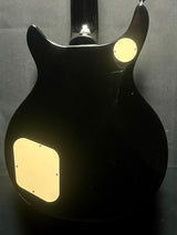 Black electric guitar with gold pickguard on a gray background