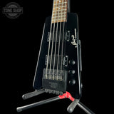 A black Spirit 4-string electric bass guitar with a natural wood fretboard, displayed on a stand against a black background. The Tone Shop logo is visible in the top-left corner.