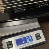 A close-up of a digital scale displaying the weight of a black bass guitar body, with the scale showing 7.89 lbs and the scale brand Weightworks visible.