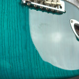 Close-up of a turquoise electric guitar with a metal bridge and pickguard.