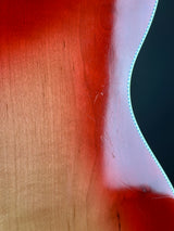 Close-up of a glossy wood surface with a wavy red-orange painted edge and visible scratches on the wood.
