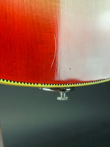 Close-up of a glossy red-orange wooden surface with a small silver metal knob and a black-and-yellow edge detail against a dark gray background.