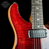Close-up of a red electric guitar with a black pickguard on a dark background.