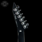 Close-up of the headstock of a black electric guitar against a black background, showing six silver tuning pegs and white printed text including 'Tone Shop' and 'Masters by Gibson'.