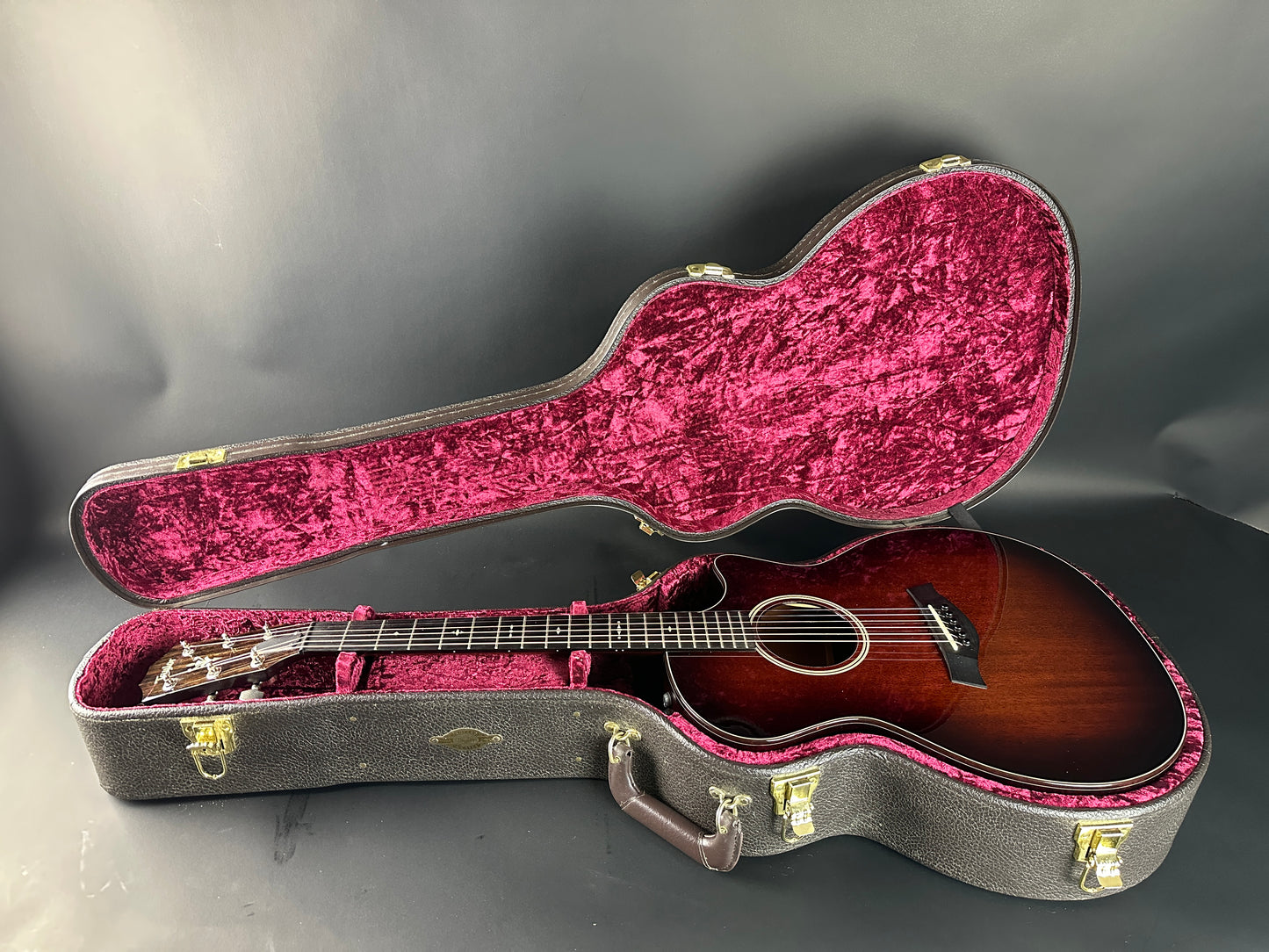 Acoustic guitar in an open case with red interior on a gray background