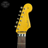 Close-up of a Fender Stratocaster electric guitar headstock in a natural yellow finish, showing six silver tuning pegs and the Fender logo, set against a solid black background.