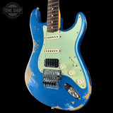 A blue and mint green electric guitar with a distressed finish, shown against a black background. The brand is identifiable as a Fender Stratocaster style guitar.