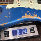A blue electric guitar body resting on a digital scale displaying 8 lb 2.4 oz, with visible distressed gold paint showing through the worn finish.