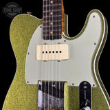Close-up of a Fender Telecaster-style electric guitar body in a metallic gold glitter finish with a white pickguard, cream humbucker pickups, and a dark fretboard, shown against a black background with a Tone Shop watermark.