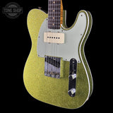 A close-up of a glittery gold electric guitar body with a white pickguard, cream humbucker pickups, and black control plate, shown against a black background with a Tone Shop watermark in the top left.