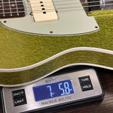 A close-up of a gold glitter electric guitar body resting on a digital scale showing a weight of 7 lbs 58 oz.
