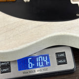 Close-up of a digital kitchen scale displaying the weight of a guitar body in ounces and pounds, with the scale showing 6.104 lbs and 6.