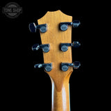 Close-up of a guitar headstock with six black tuning pegs and a natural wood finish, shown against a black background with a Tone Shop watermark in the top left corner.