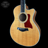 A Taylor acoustic-electric guitar with a natural wood body, dark fretboard, and red pickguard, shown against a solid black background with a Tone Shop watermark in the top left corner.