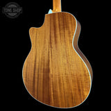 The back of an acoustic-electric guitar with a rich wood grain finish, shown against a solid black background with a Tone Shop watermark in the top-left corner.