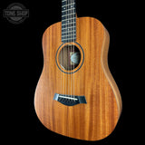 A close-up of an acoustic guitar body made of warm honey-toned wood with a black soundhole ring, bridge, and fretboard, shown against a solid black background. A 'TONE SHOP' watermark is visible in the top-left corner.