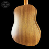 The back of an acoustic guitar made of polished wood, showing a warm golden-brown grain pattern, set against a solid black background with a Tone Shop watermark in the top left corner.
