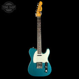 Blue electric guitar with a white pickguard on a black background, featuring the Tone Shop logo.