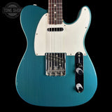 Blue electric guitar with a white pickguard on a black background, featuring the Tone Shop logo.