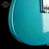Close-up of a teal electric guitar with a 'Tone Shop' logo in the corner.