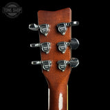 Close-up of a guitar headstock with six silver tuning pegs branded Tone Shop, set against a solid black background.