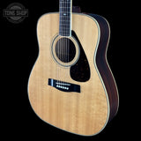 An acoustic guitar with a natural wood top and dark sides, shown against a solid black background with a Tone Shop watermark in the top-left corner.