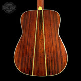 The back of an acoustic guitar made of rich, dark brown wood with a gold-colored inlay running down the center, set against a solid black background. A Tone Shop watermark is visible in the top-left corner.
