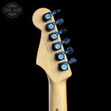 Close-up of the headstock of a Fender electric guitar, showing the natural wood neck, six black tuning pegs with light blue circular dials, and a Tone Shop watermark in the top left corner against a black background.