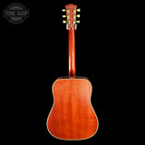 The back of a wooden acoustic guitar with a glossy reddish-brown finish and gold tuning pegs, shown against a solid black background with a Tone Shop watermark in the top-left corner.