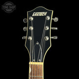 Close-up of a Gretsch acoustic guitar headstock against a black background, showing the Gretsch logo, six silver tuning pegs, and part of the wooden fretboard.