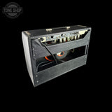 A black guitar amplifier head with its front grille removed, showing the internal speaker and control panel, photographed against a solid black background. A 'Tone Shop' logo watermark is visible in the top-left corner.