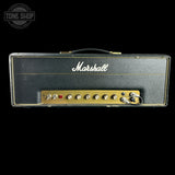 A vintage Marshall guitar head amplifier head against a solid black background, featuring its signature black textured cover, gold trim, white script logo, and gold control panel with knobs and a lock.